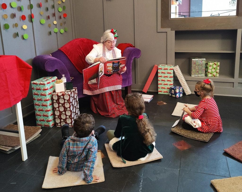 Mr.s Claus in a big red chair reading to children sitting on the floor at Capital Mall