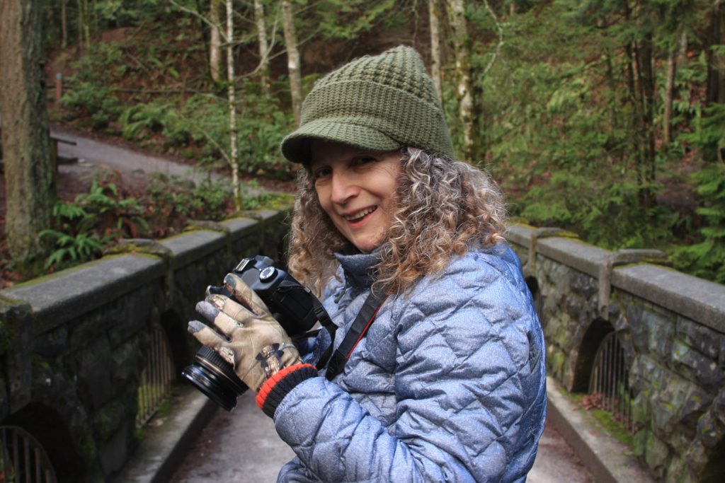Bus driver Deana Ready standing on a wooded bridge with a camera in her hand