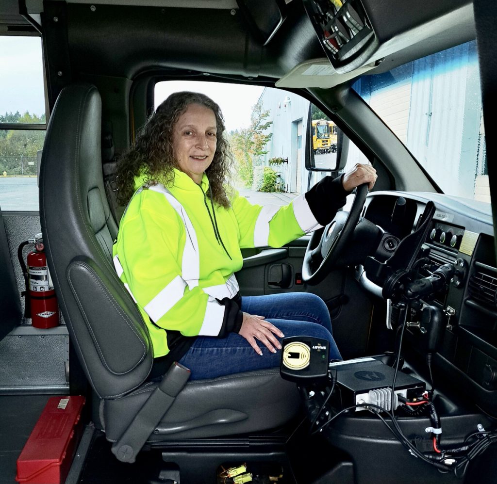 Deana Ready sitting her school bus driver's seat with a bright neon yellow jacket on