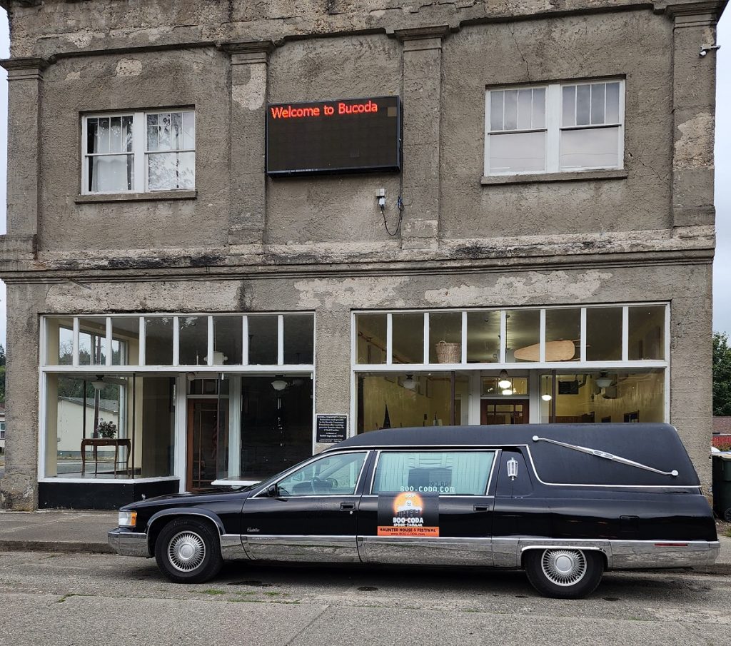 Hearse outside a building with writing on it that says 'BOO-CODA'