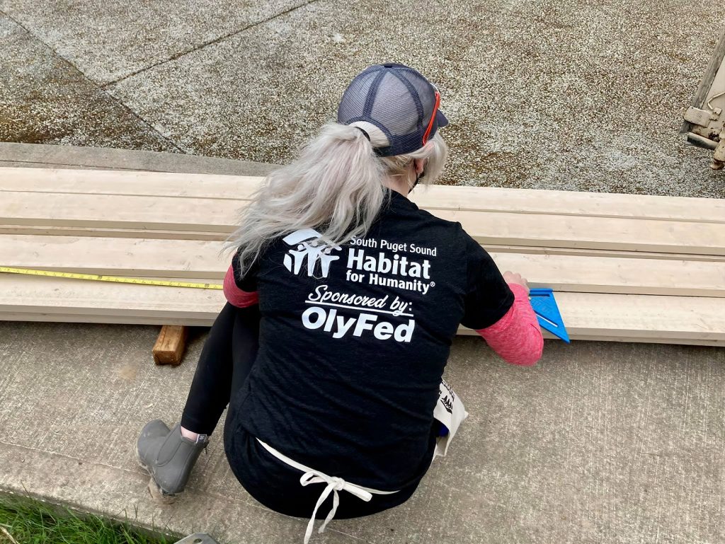 woman kneeling over a pile of boards with a Habitat for Humanity/OlyFed shrit on