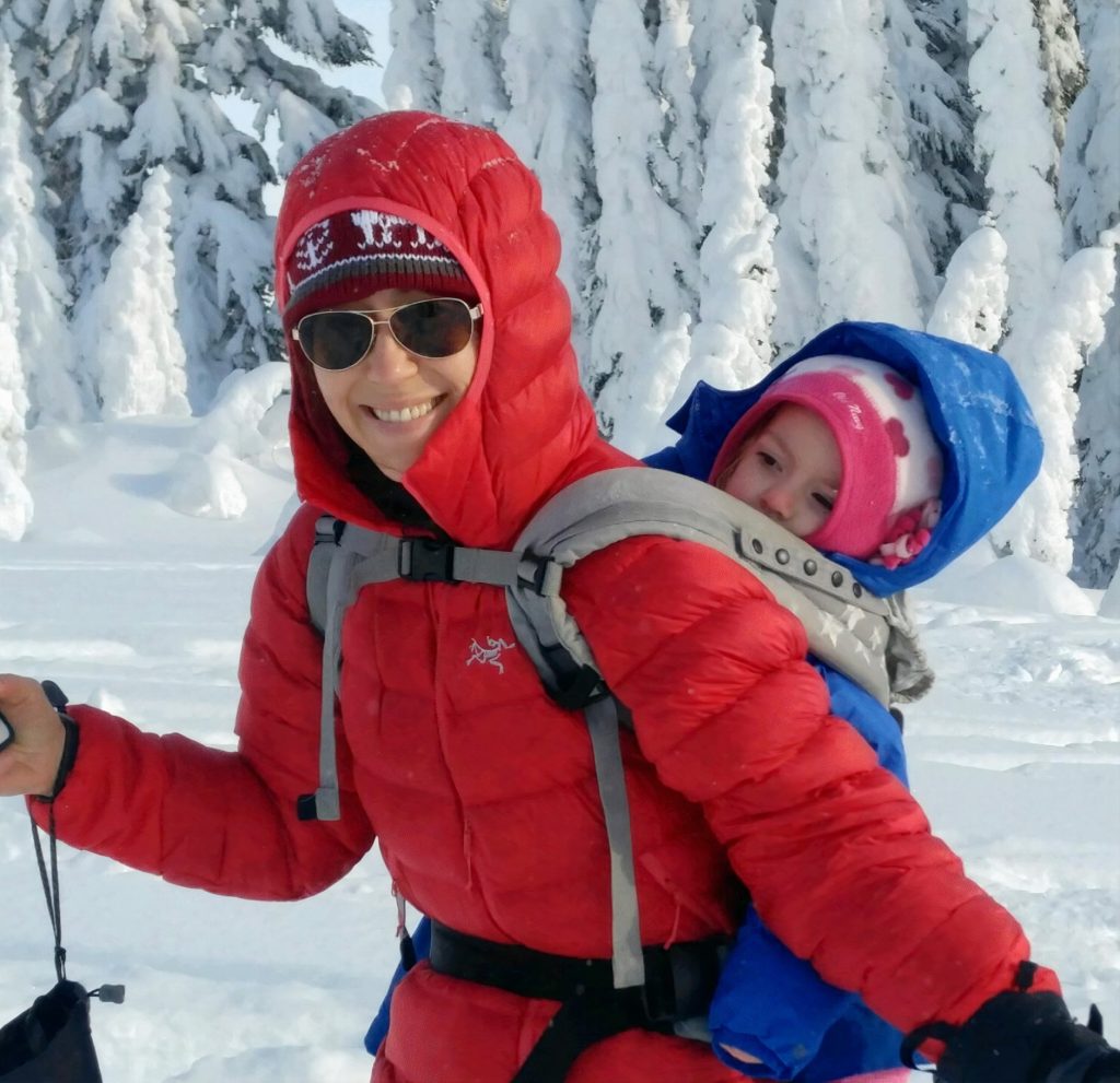 Sheila Smitherman cross country skiing with a baby on her back in a snow-covered wood