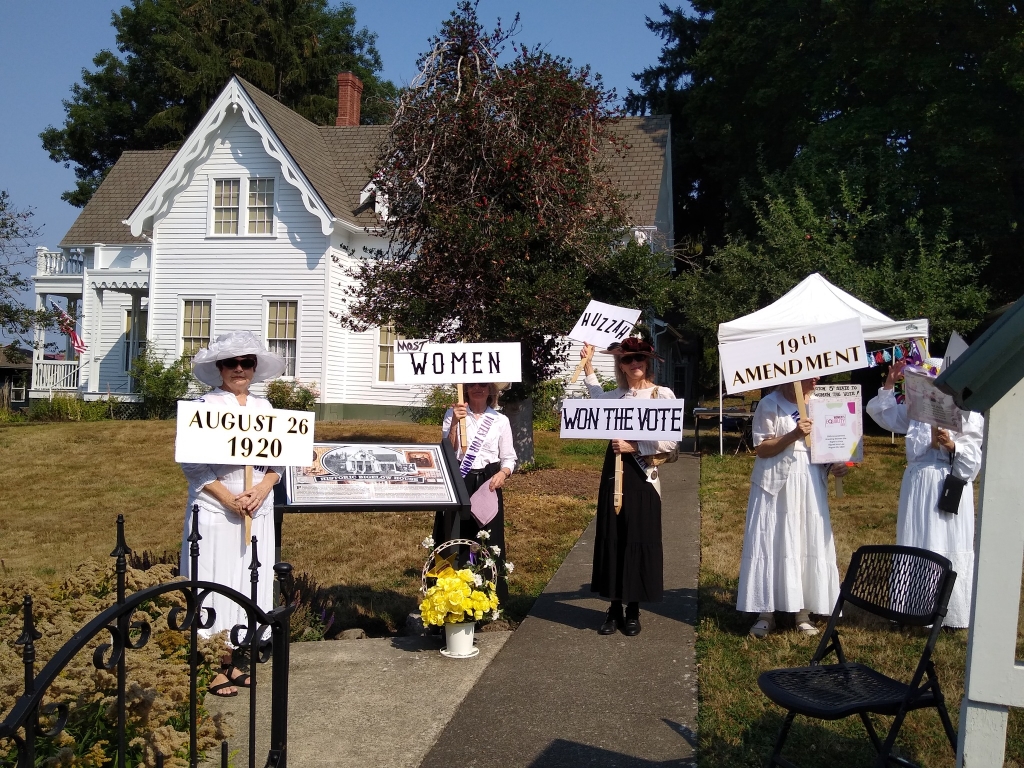 Women dressed up in 19th century white dresses with woman suffrage signs.