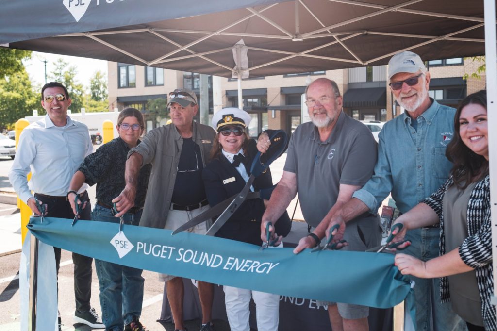 people at the Olympia Yacht Club ribbon cutting for their new EV Charging station behind a big teal ribbon