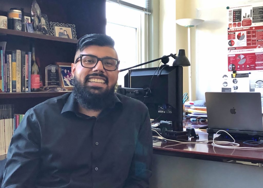 Aman Lidder sitting at a desk and smiling at the camera