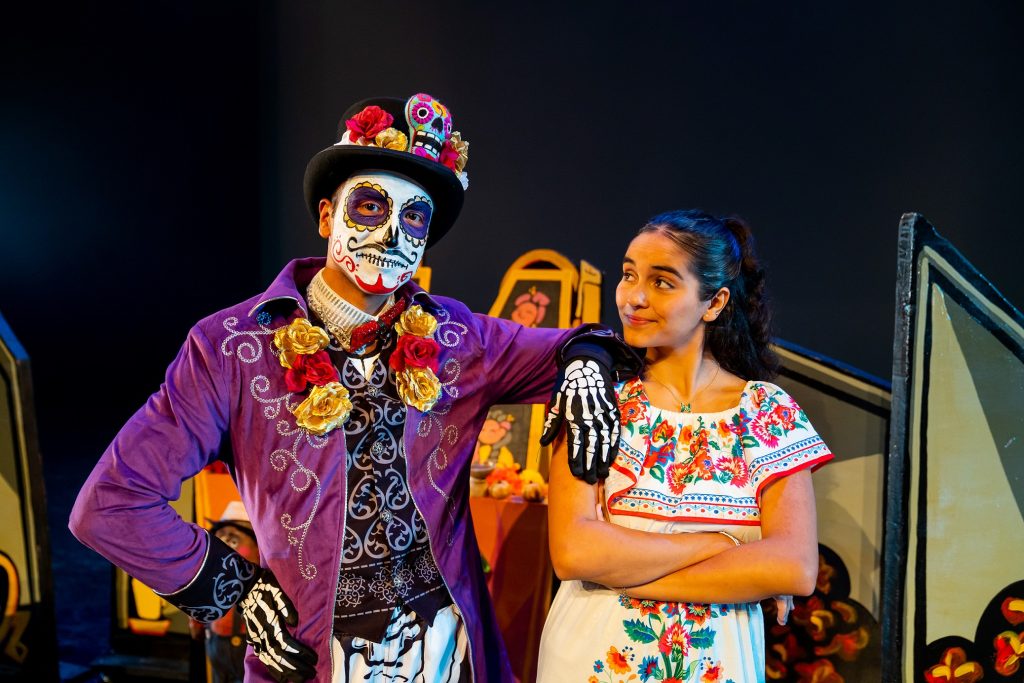 A woman in a traditional Mexican dress stands with a man dressed in a Sugar Skull costume