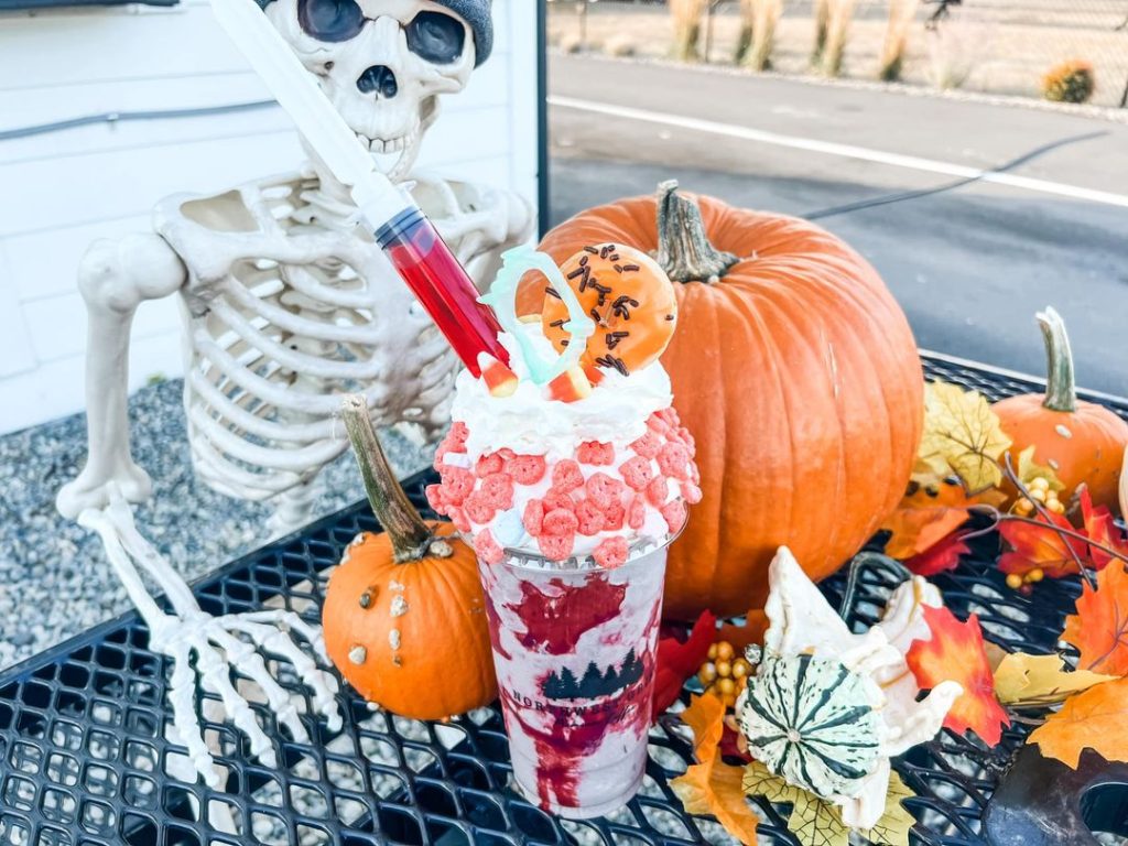 Blended cookies and cream drink with strawberry puree, whipped cream and a donut on top sitting on a table with a skeleton, pumpkins and fake leaves
