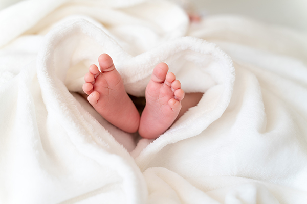 tiny, cute, bare feet of a little caucasian newborn baby girl/boy wrapped in a heart shaped white soft and cosy blanket, symbolizing love