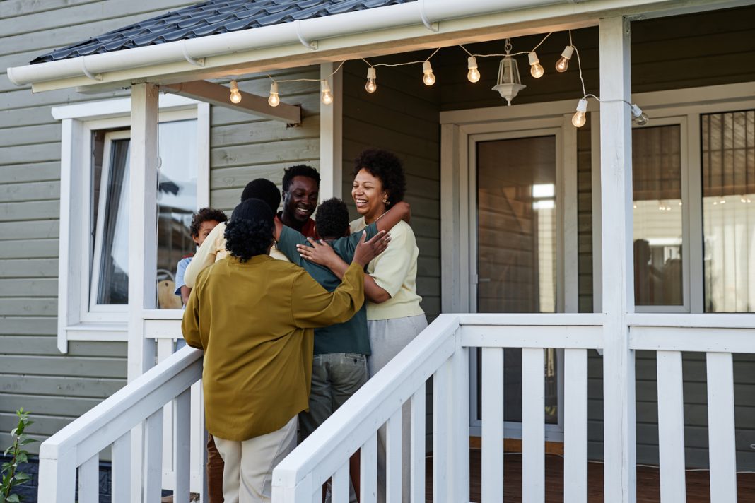 Portrait of happy black family embracing while standing on porch of new house