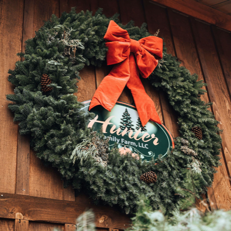 Big greenery wreath on a barn wall with a sign in the middle that says, 'Hunter Family Farm'