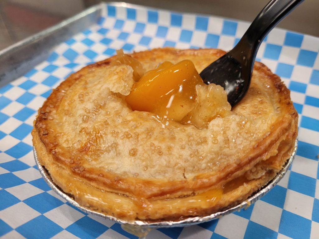 peach pie with a serving utensil in it on a blue and white checked tablecloth