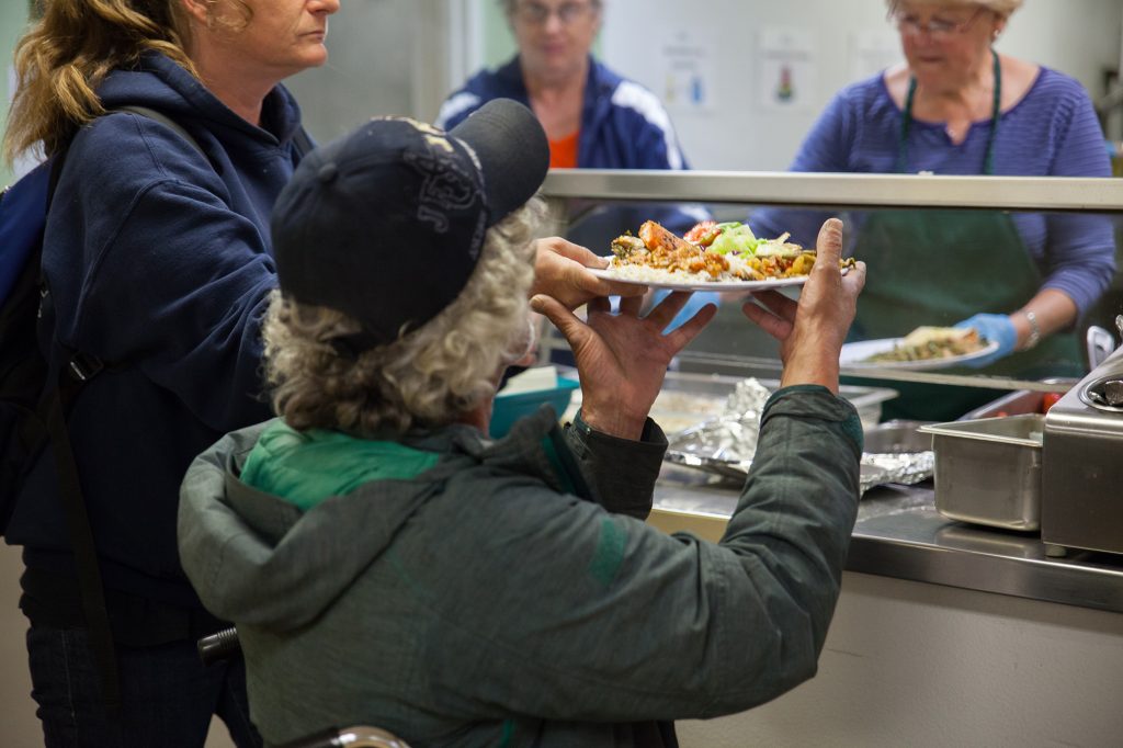 a person takes a plate of food from a food kitchen volunteer