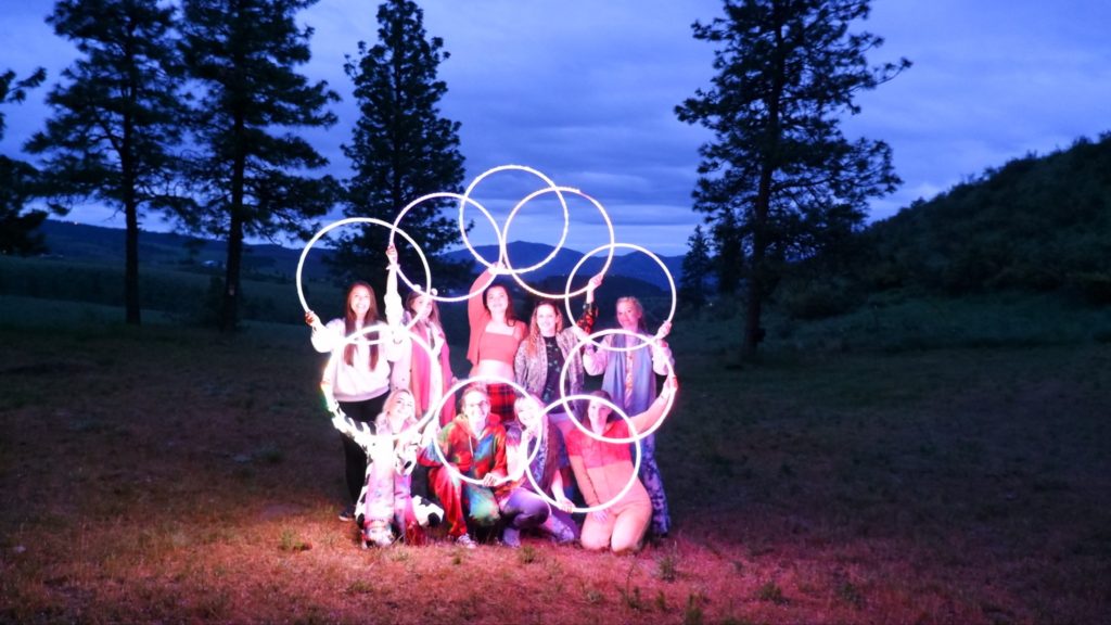 a group of woman posing for a photo at dusk holding light up hula-hoops