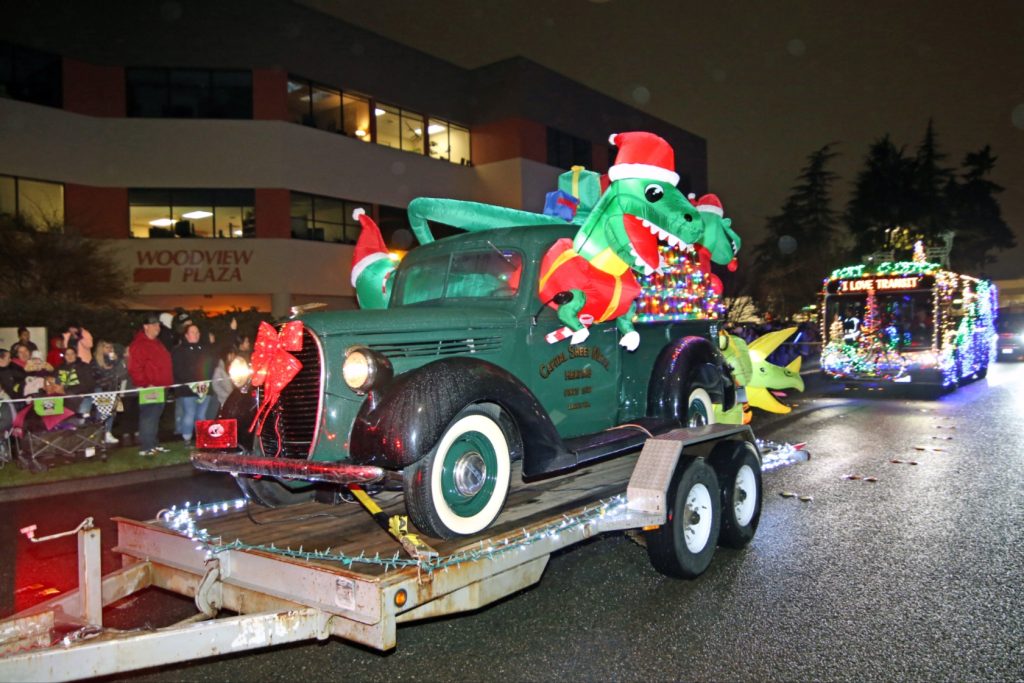 City of Lacey lighted tree parade entry - a vintage truck on a flatbed with inflatable t-rexs inside and a christmas tree in the bed.
