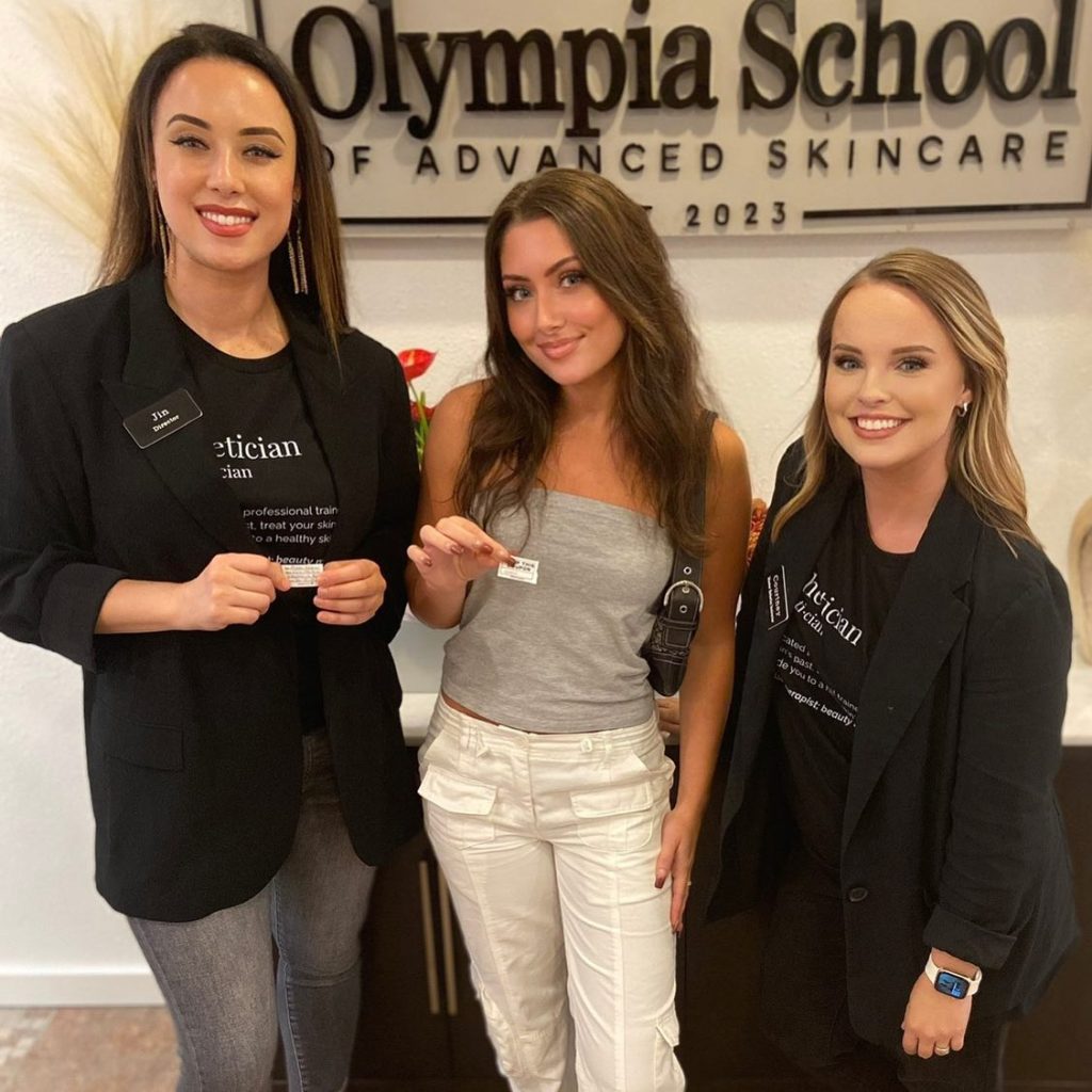 Three woman pose for a photo in front of the Olympia School of Advanced Skincare sign.