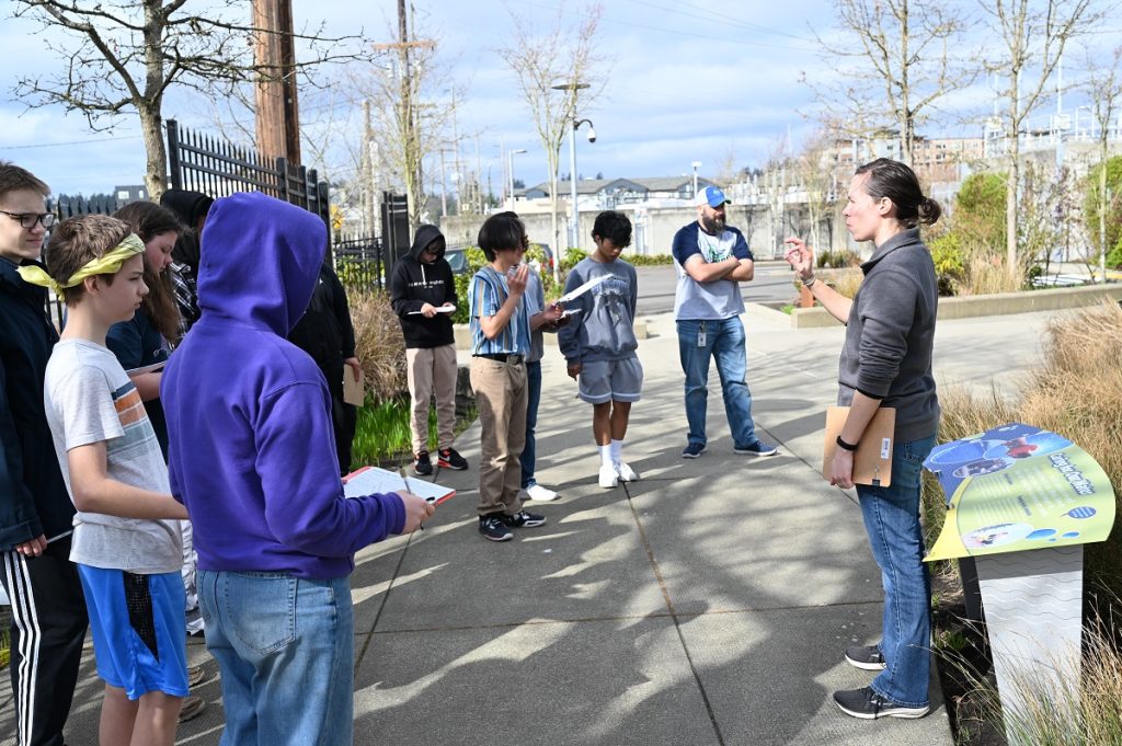 Kids standing outside on a sidewalk listening to a speaker