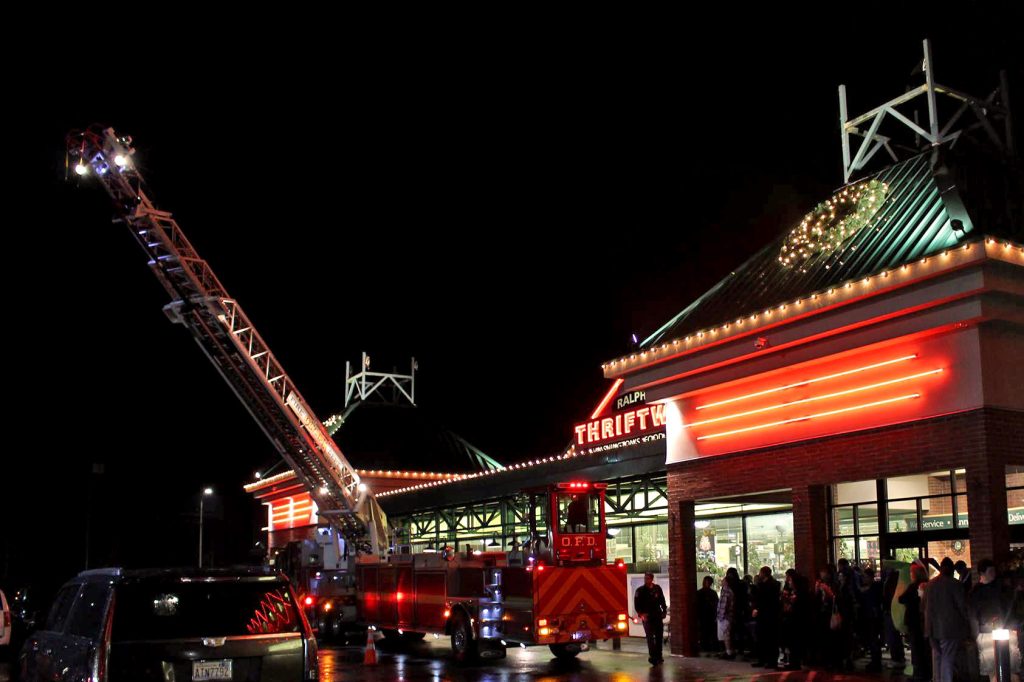 a fire truck with it's ladder up outside Ralph's Thriftway at night with christmas lights up on the building