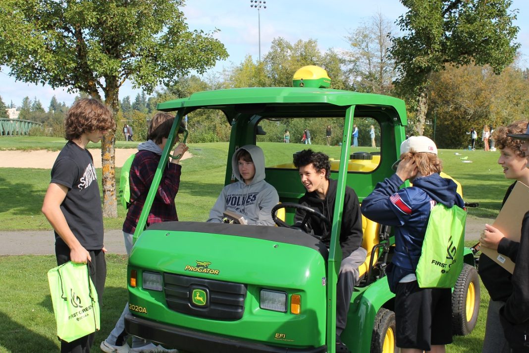 Teenagres by a green golf cart. Each is carrying a bright green bag, one is in the cart.