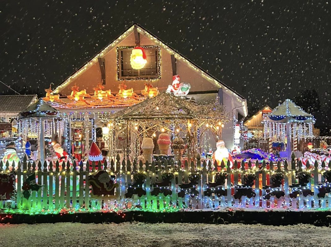 house covered in multicolored christmas lights with lots of Christmas displays in the yard.