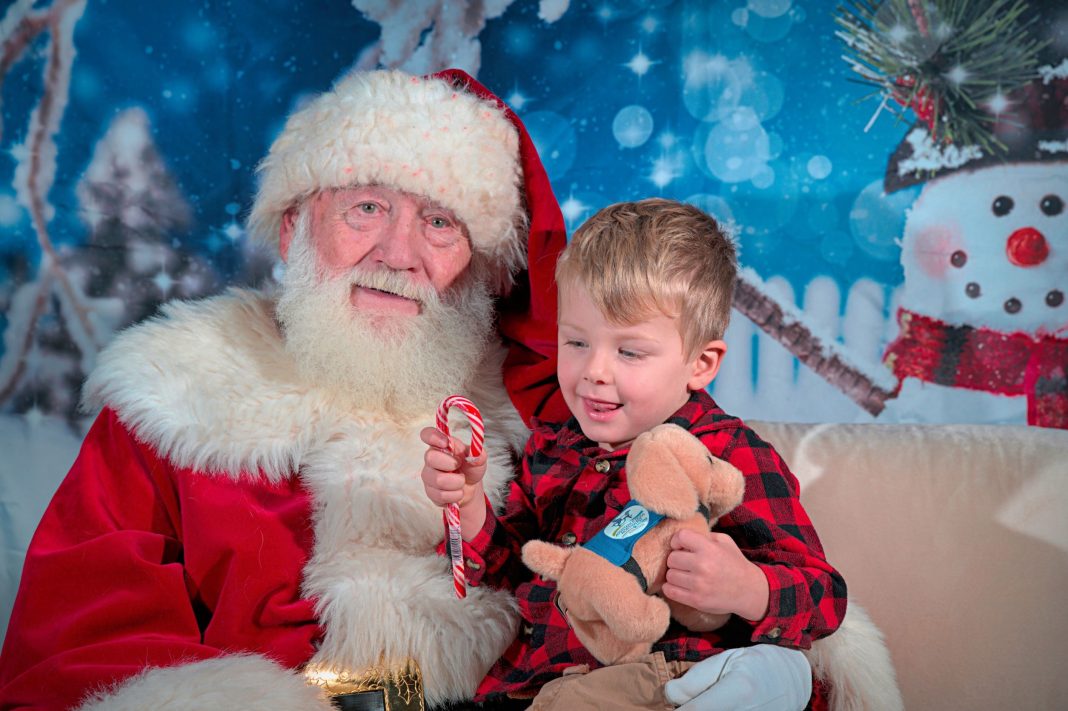 young boy sitting on Santa's lap with a candy cane and a stuffed animal