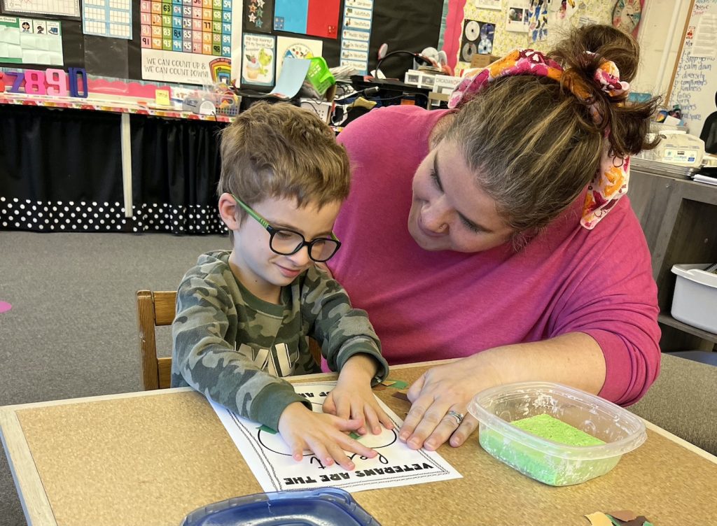 Holly Johnson kneeling by a student who is working on a worksheet