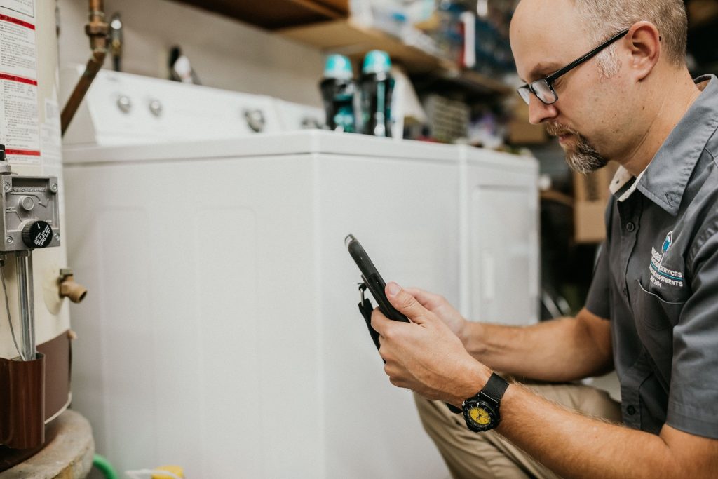 Boggs technician kneeling by hot water heater looking at a phone