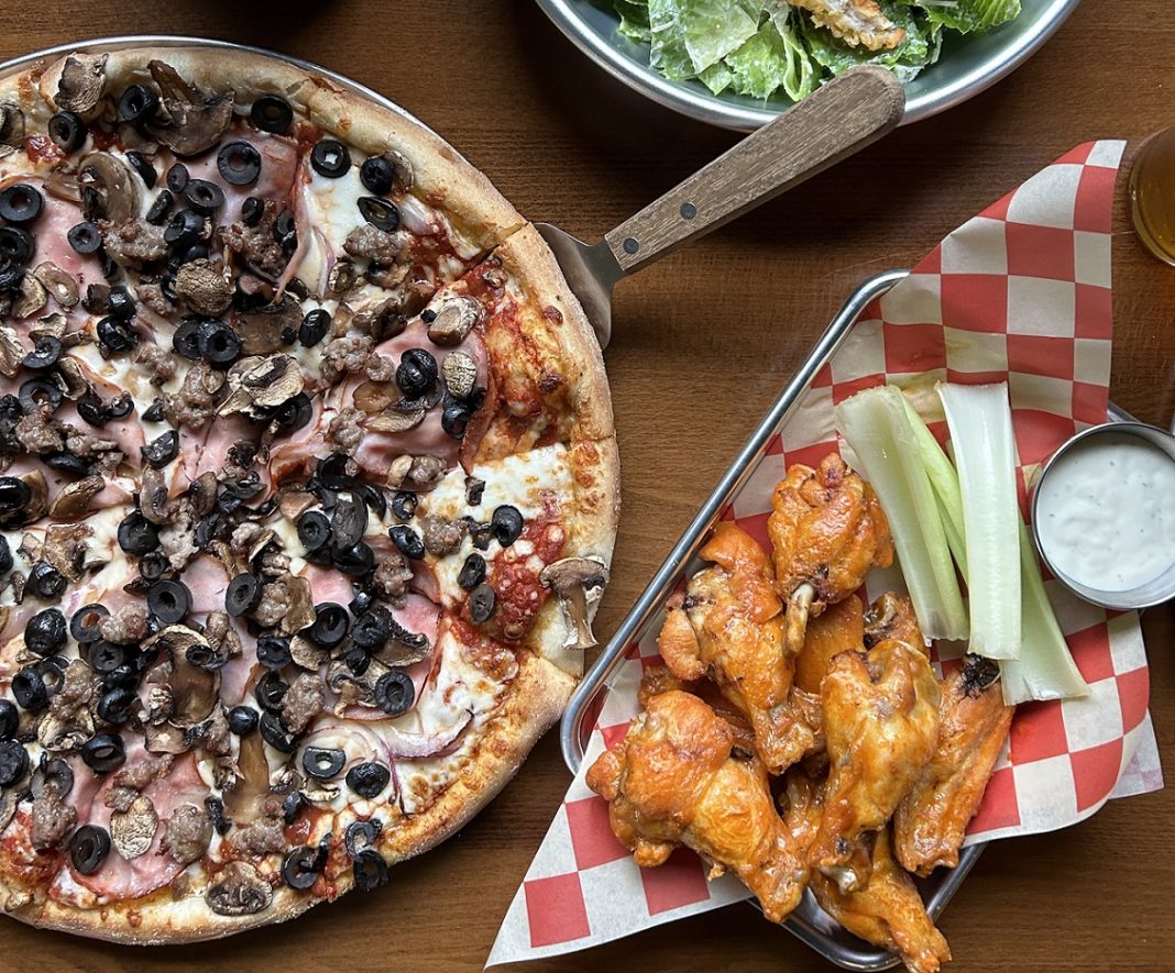 pizza with canadian bacon, mushrooms and black olives with a salad and chicken wings on the side