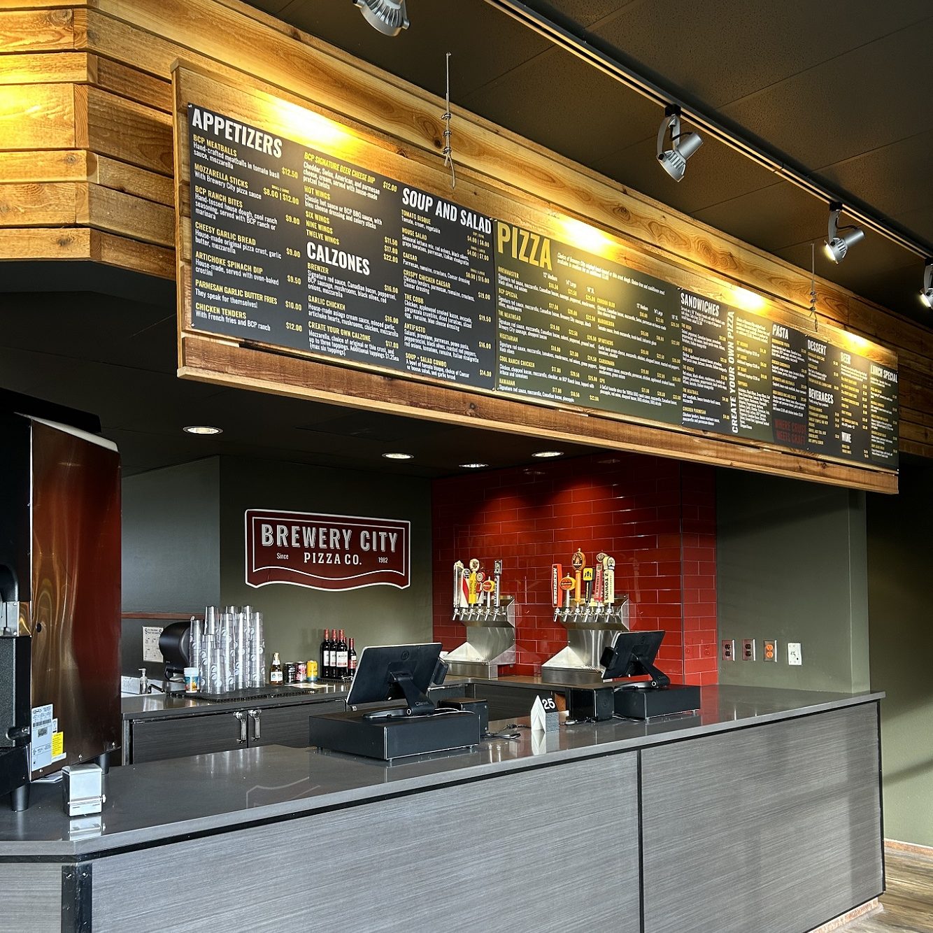 Brewery City Pizza front ordering area with a cash register on the counter and a menu on the wall above it