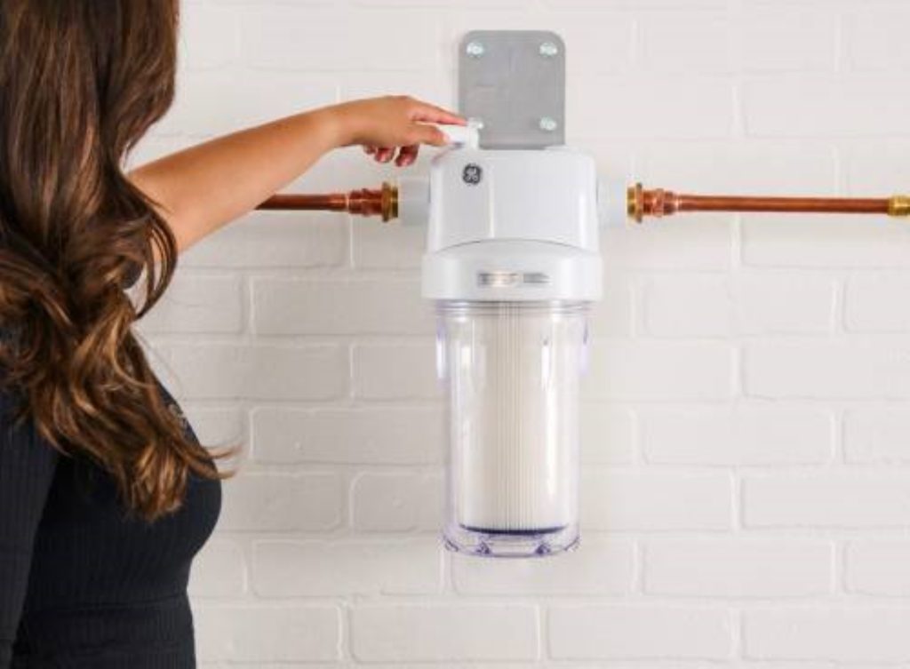 a woman has her hand on a water treatment container connected to two brass pipes