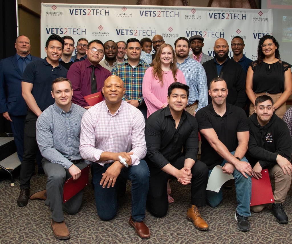 group of people posing for a photo in front of a step and repeat that says 'Vets2tech'