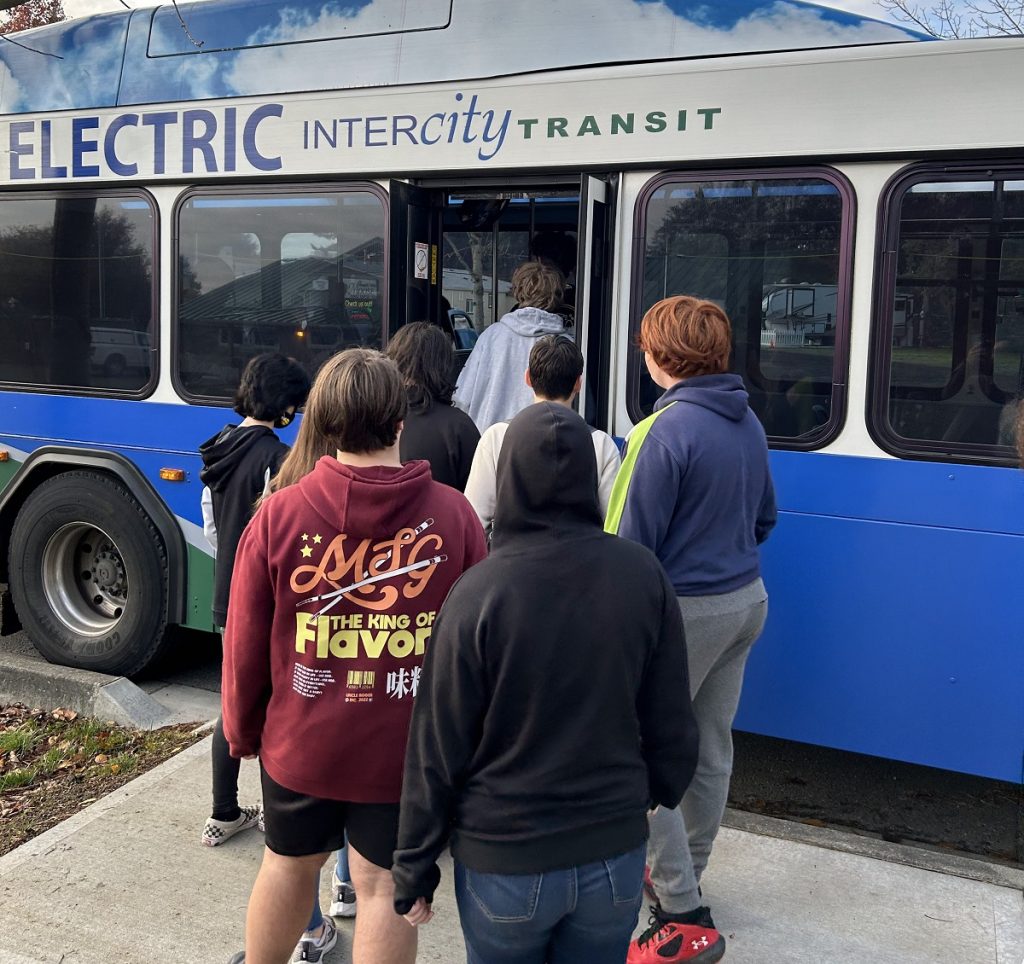 high school students standing in a line to get on a city bus that says, 'electric intercity transit'