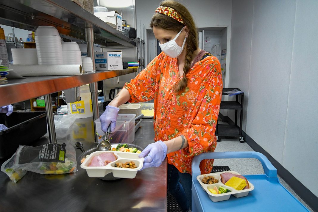 a woman serves up food into a plastic serving trays.
