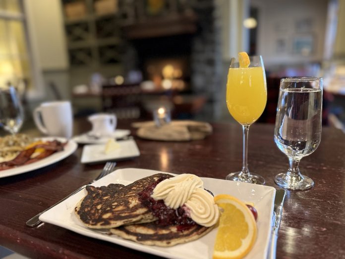 pancakes with butter and an orange slice and a mimosa on a wood table