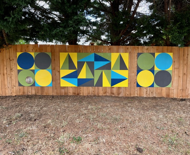 circles and triangles in yellows, blues and black on a cedar fence