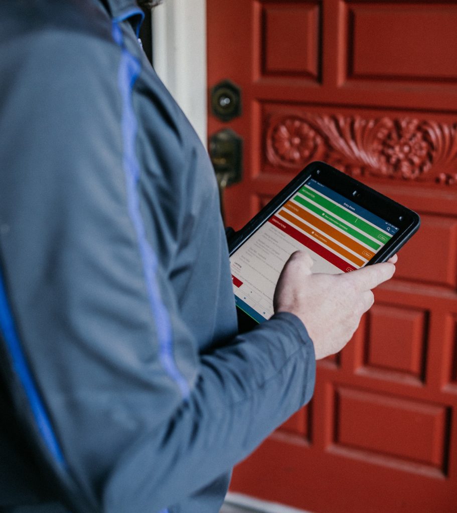a man stands in front of a red door holding a tablet in his hand