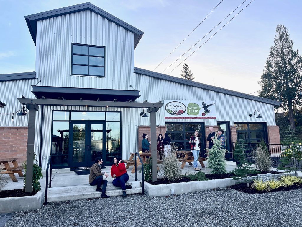 white building with Finnriver Cidery banner on the front and people standing and sitting outside