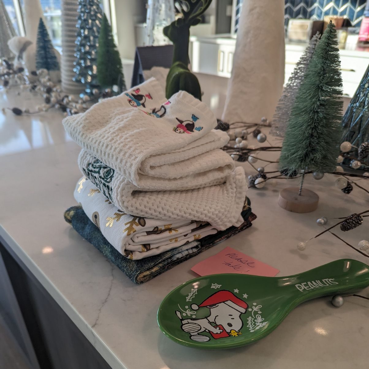 christmas trees, holiday towels, a spoon rest with Snoopy in a santa hat and other decorations on a white counter top