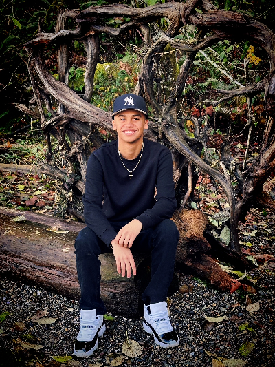 Joel Galarza Jr. sitting on a log in the woods