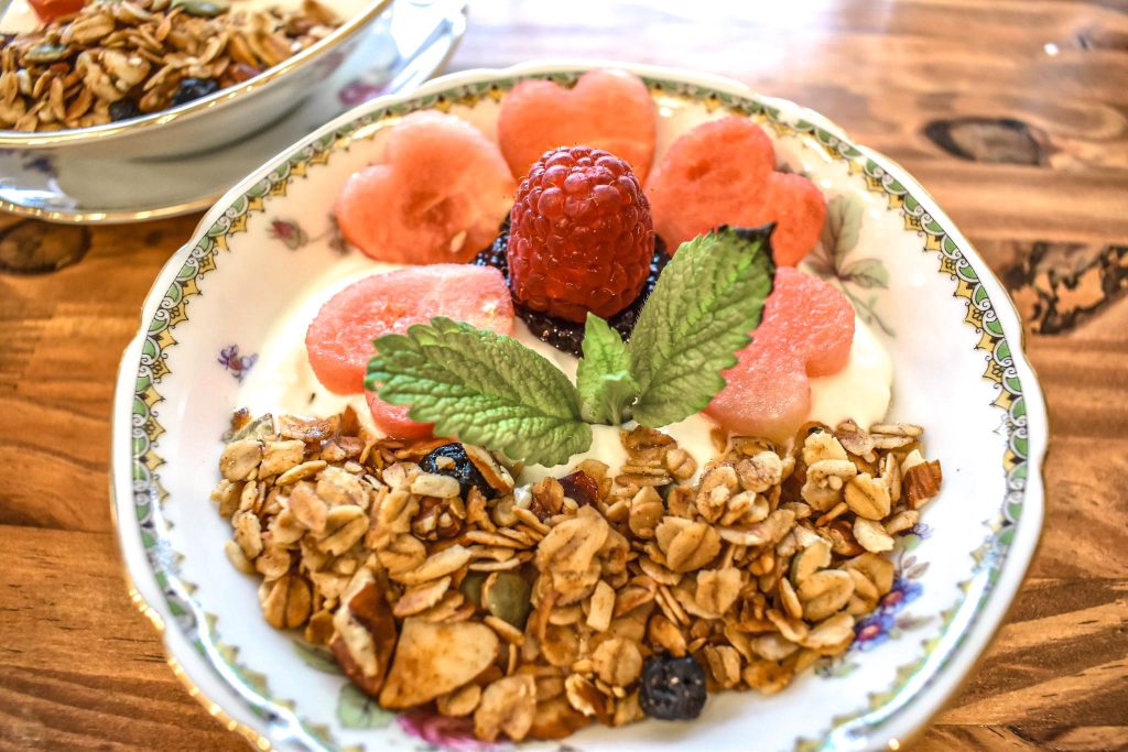 granola and yogurt in a bowl with heart shaped red melon, a sprig of mint and a raspberry