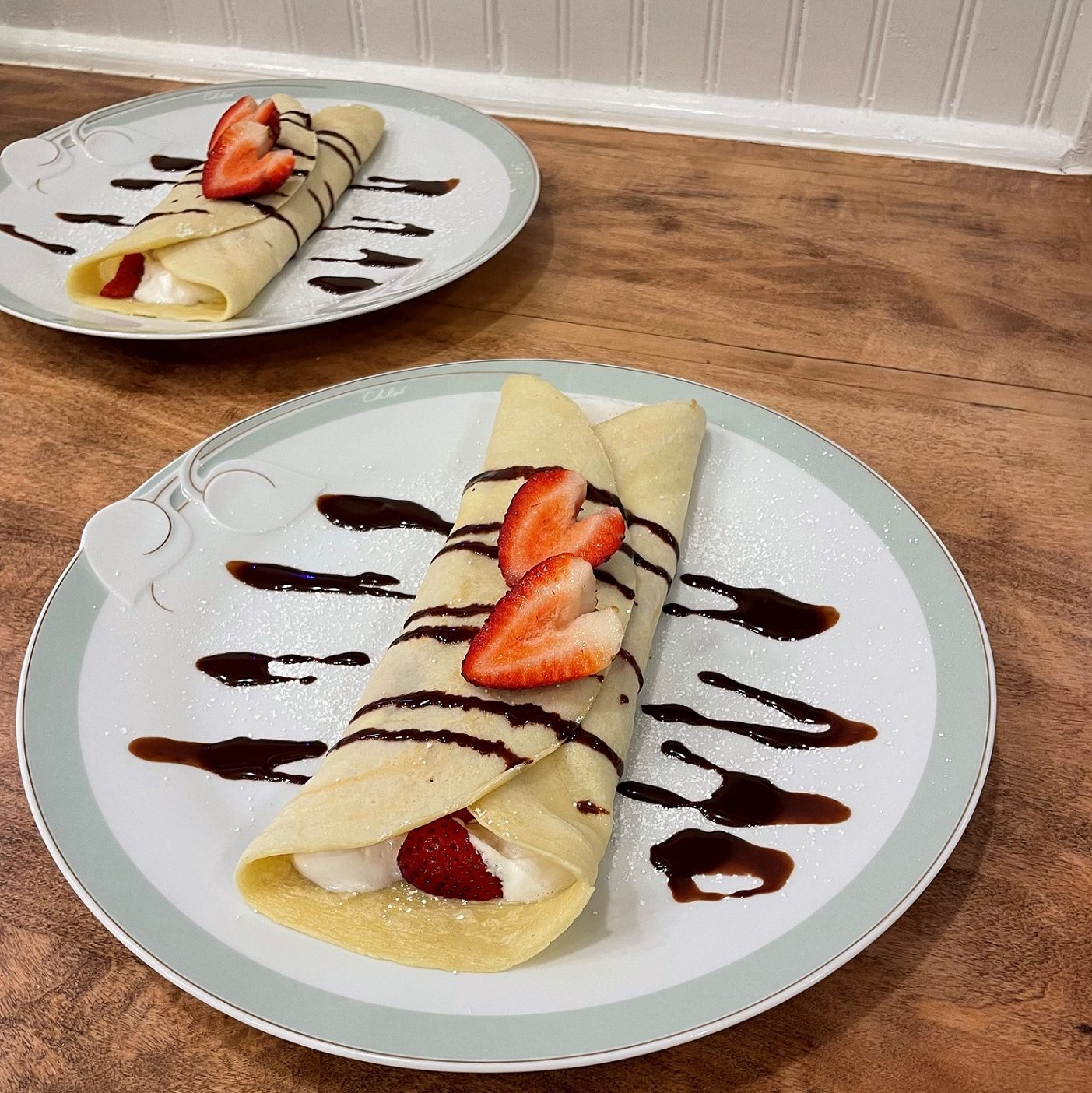 crepes on white plates with strawberries and chocolate drizzle