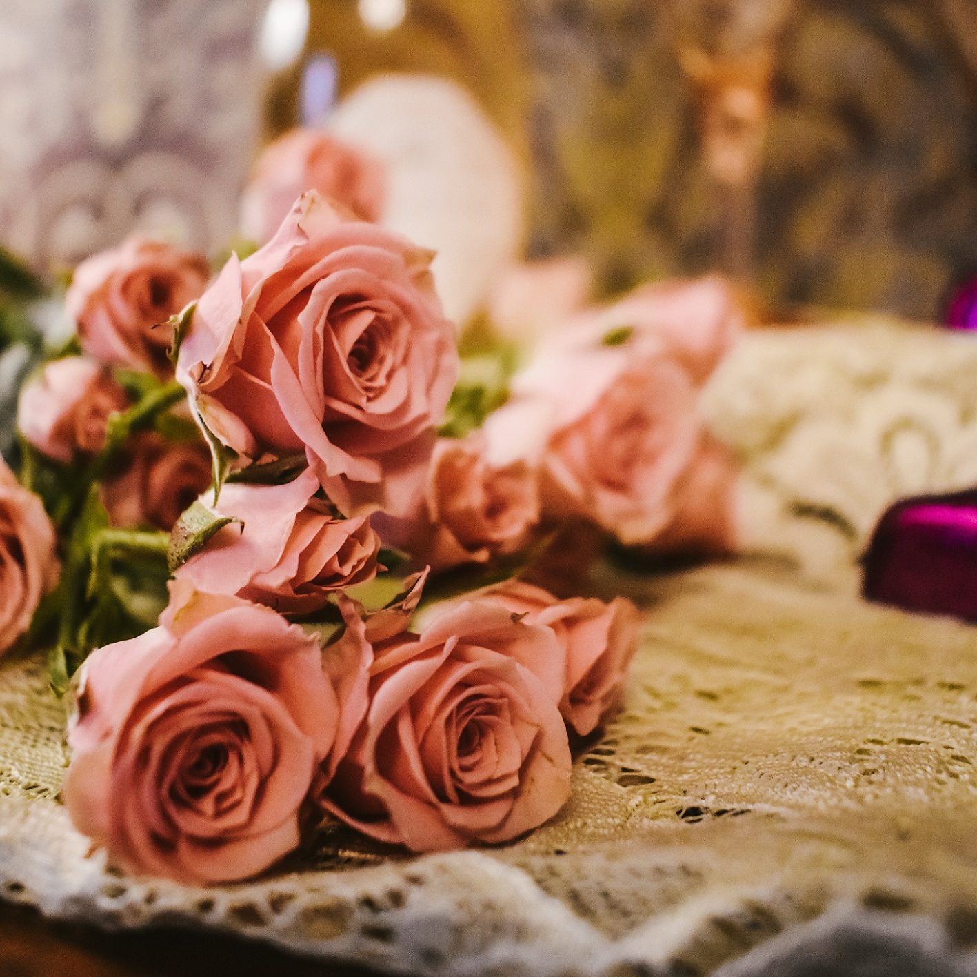 close up of a bundle of pink roses on a white lace tablecloth