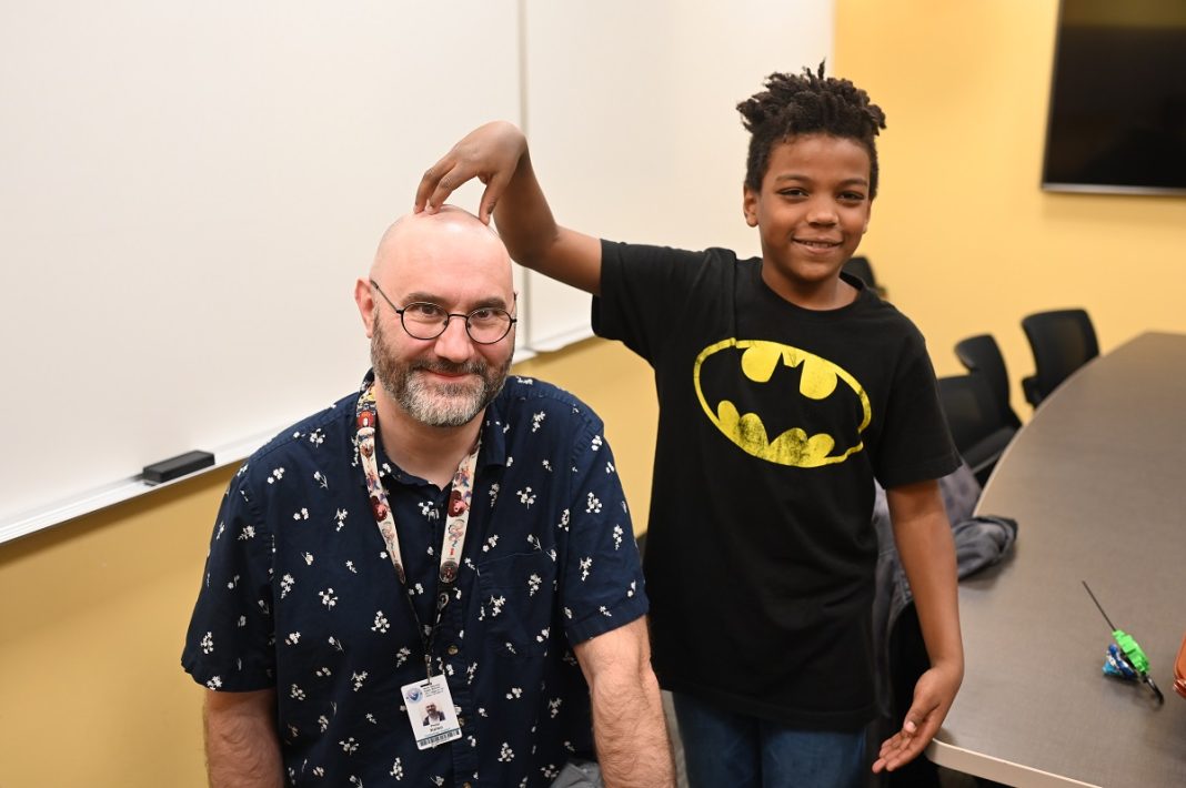 a man sitting in a chair while a male child stands next to him with his hand on the man's head.