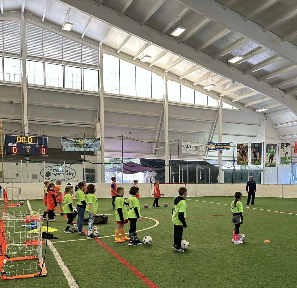 young kids in bright yellow and orange jerseys on an indoor soccer field