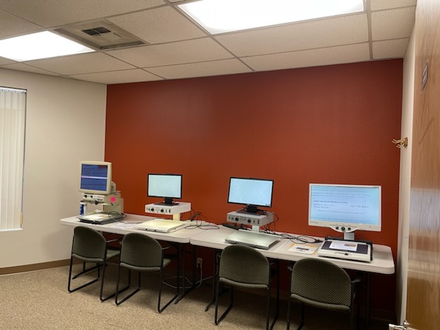 a row of computers on a long desk with four chairs in front of a russet-colored wall