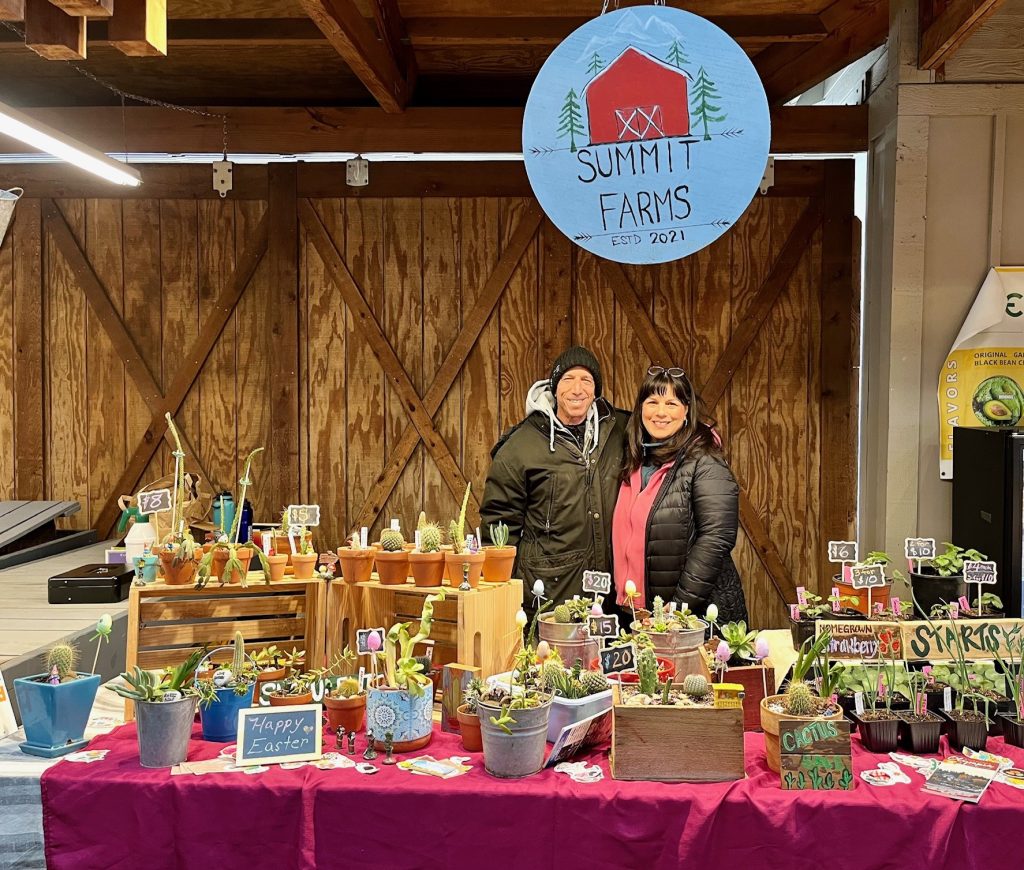 Mitch and Michelle Lewis standing behind a table full of plants for sale with a sign above their heads that says, 'Summit Farms estd 2021'