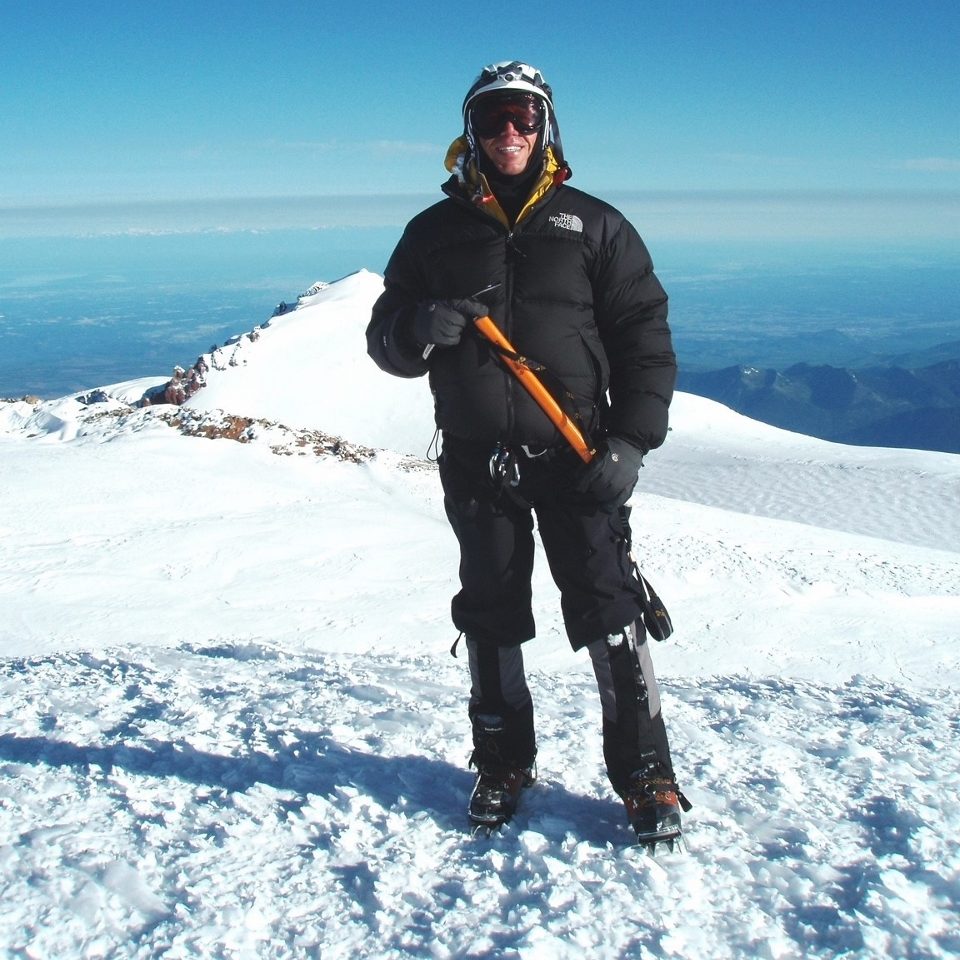 Mitch Lewis standing on a mountain top covered in snow holding a pickax