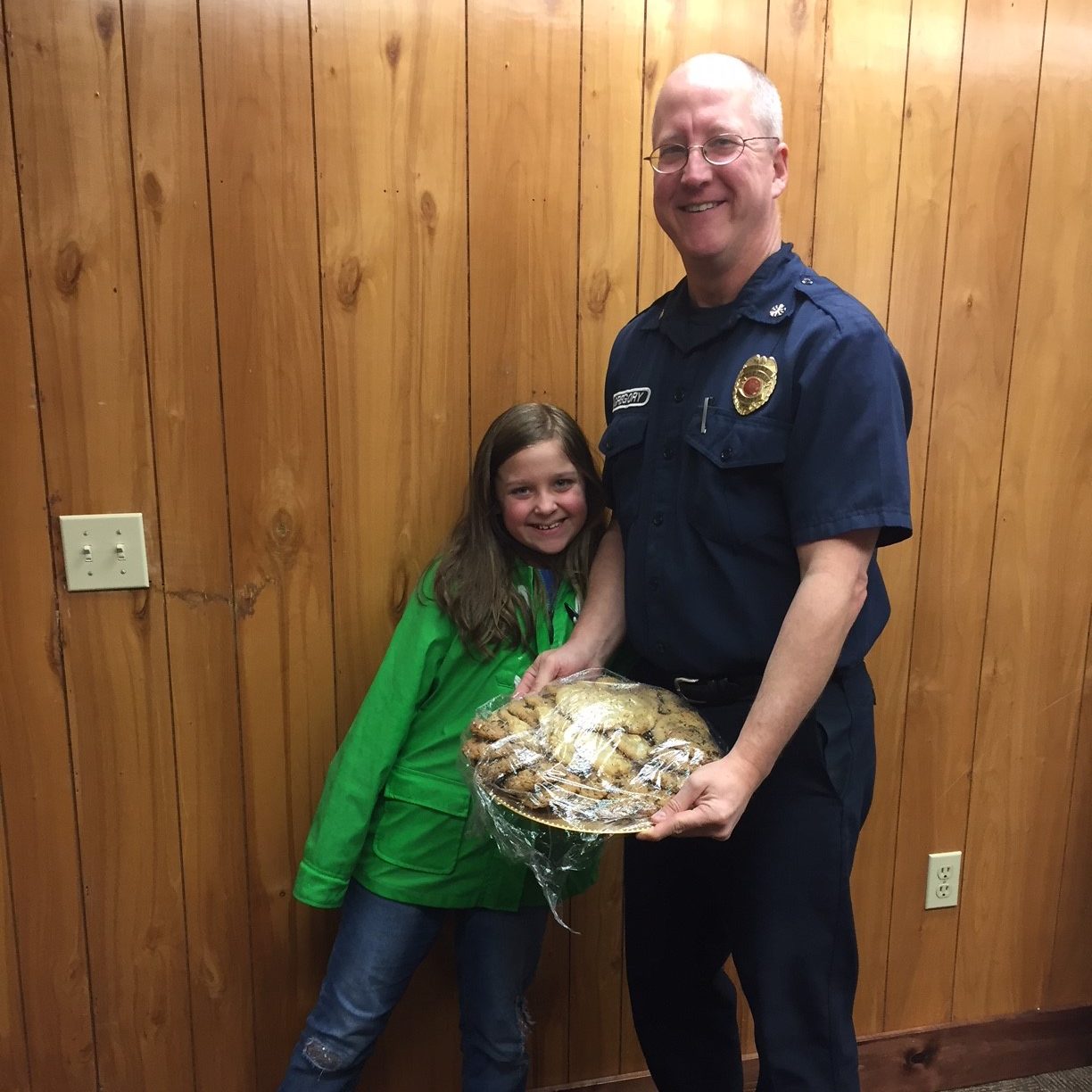 a young student hugs a firefighter who is holding a plate of cookies