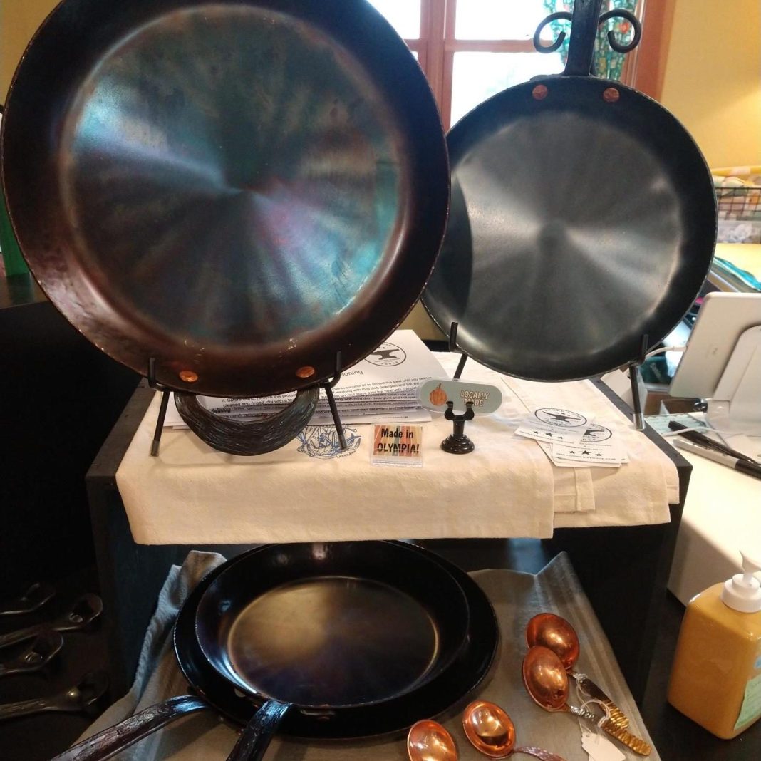 frying pans on display on top of fabric placemats with business cards and copper measuring spoons next to them