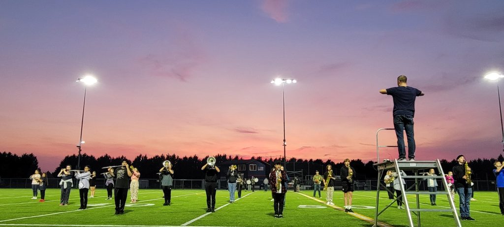 school band performing at sunset on a football field