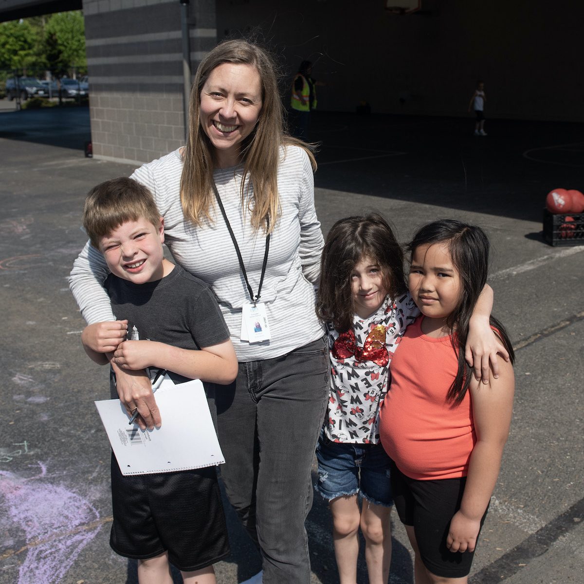 a woman hugs one kid and has two other kids standing next to her on a sidewalk